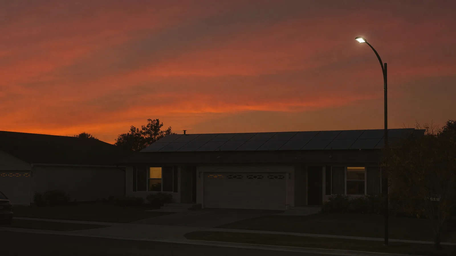 Australian suburban home at dusk with rooftop solar panels silhouetted against an orange twilight sky